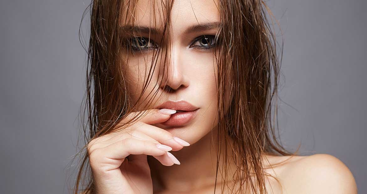 Modelo com cabelo molhado e olhar penetrante com dedo nos lábios